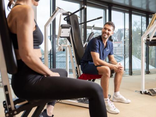 Trainer im ArenaVita Fitnessclub in Baden-Baden betreut eine Frau beim Training an den Geräten.