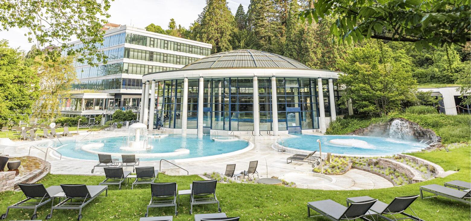 Außenansicht der Caracalla Therme in Baden-Baden mit Glasrotunde, Außenbecken und umliegender Liegewiese mit Sonnenliegen.